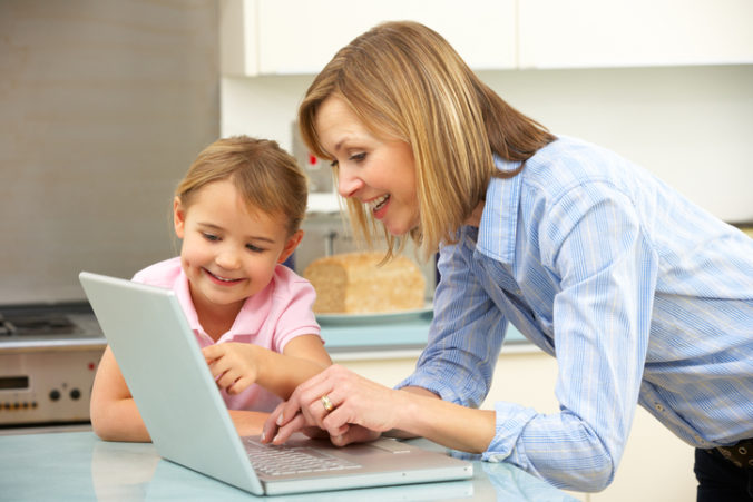 Mother and daughter using laptop in domestic kitchen at table chatting