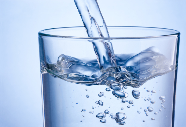 Close up pouring water into glass on a blue background