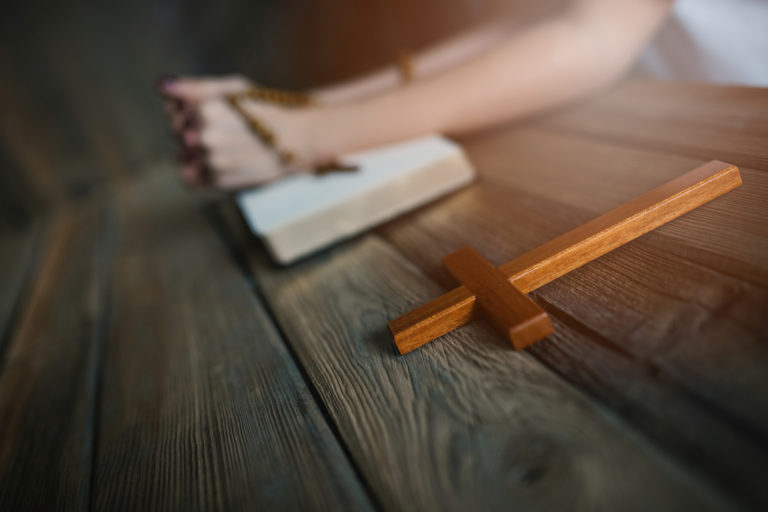 Womans hands with wooden rosary and Holy Bible