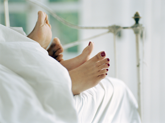 Couple lying in bed, feet sticking out of covers, low section