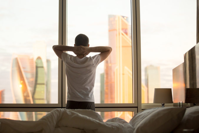Young man watching sunrise in his bedroom