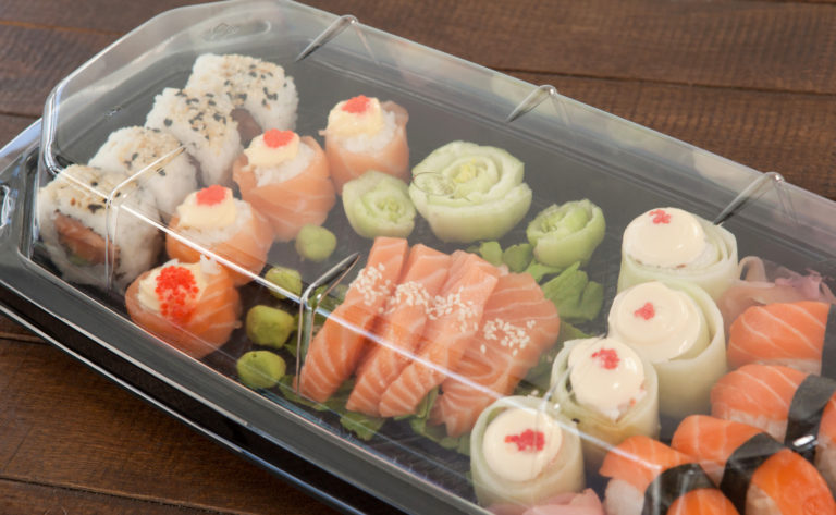 Set of assorted sushi kept in a plastic box on wooden table