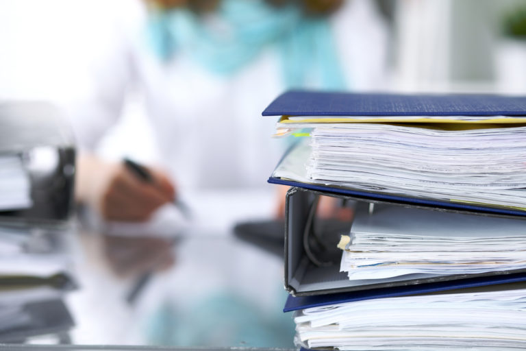 Binders with papers are waiting to be processed with businesswoman or secretary back in blur. Internal Revenue Service inspector checking financial document