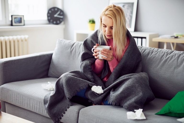 Young woman drinking tea while covered in blanket