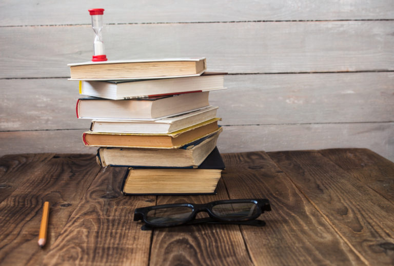 Pile of books and hourglass glasses and pencil