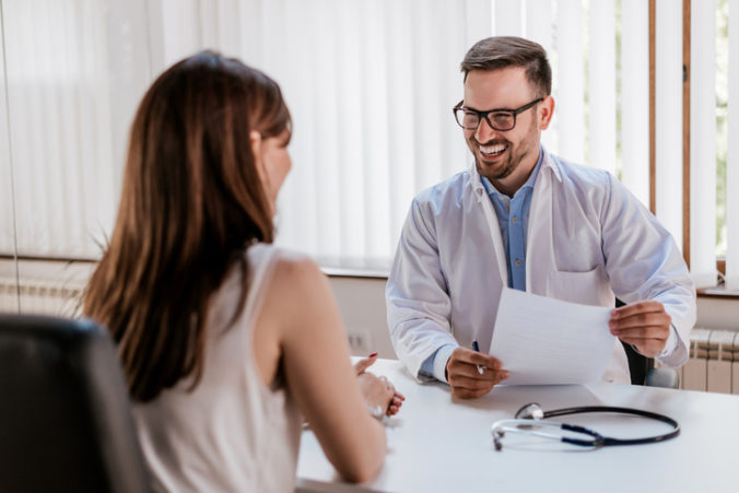 Happy male doctor discussing with patient at table in clinic