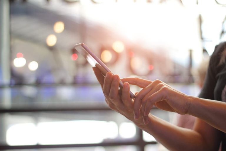 Close up of women's hands holding smartphone. Her watching sms, message, e mail on mobile phone in coffee shop. Blurred background.
