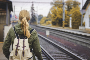 Woman with backpack standing at railroad station platform and waiting for a train. Travel concept.