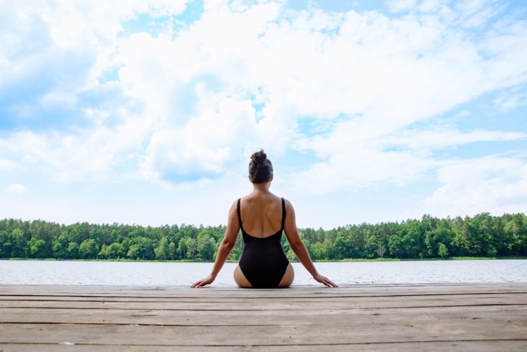 Woman sitting on wooden dock looking at lake in sunny day