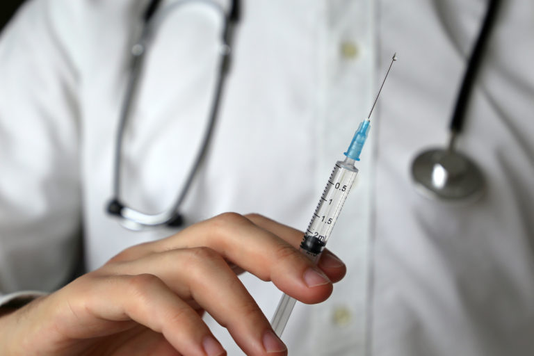 Doctor with syringe, man with stethoscope preparing to injection. Concept of vaccination, treatment in clinic, plastic surgery