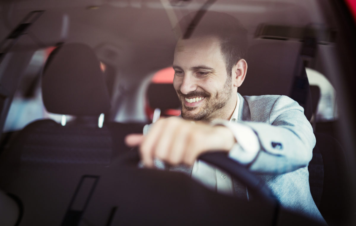 Attractive happy young man driving car and smiling