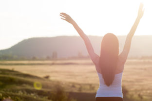 Cheering woman open arms to sunrise