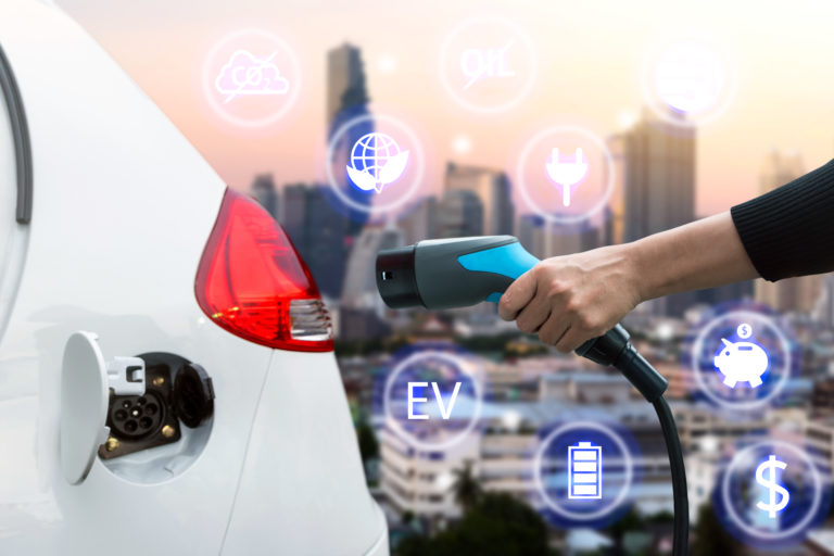 Air pollution and reduce greenhouse gas emissions concept. Hand holding and charging Electric car with blur city view background.