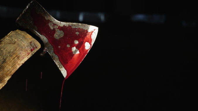 Axe with blood in hand on the dark background