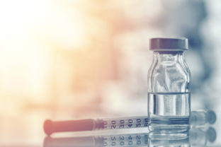 Closeup of medicine vial or flu, measles vaccine bottle with syringe and needle for immunization on vintage medical background, medicine and drug concept