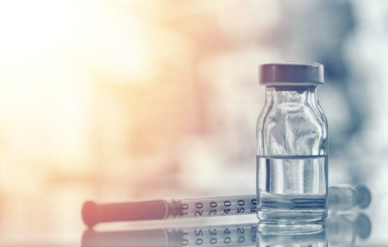 Closeup of medicine vial or flu, measles vaccine bottle with syringe and needle for immunization on vintage medical background, medicine and drug concept