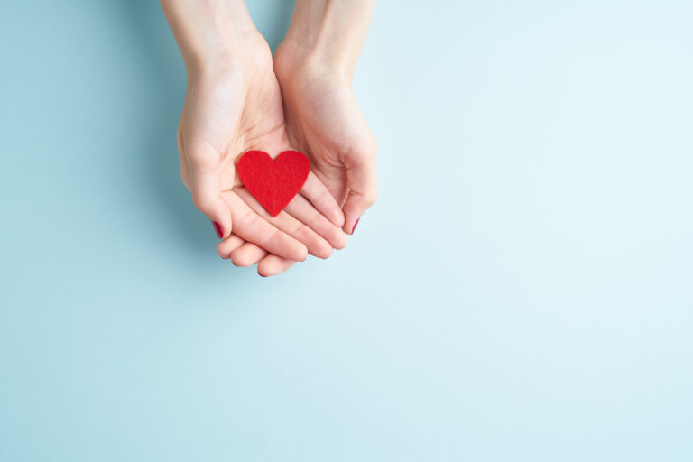 A person holding red heart in hands, donate and family insurance concept, on aquamarine background, copy space top view