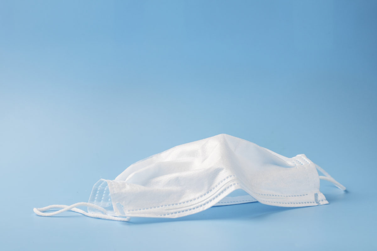 Typical 3 ply surgical mask to cover the mouth and nose. Surgical mask with rubber ear straps. Concept of medicine and healthcare, anti virus procedures. Selective focus. Copy space