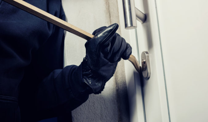 Burglar using crowbar to break a home door at night