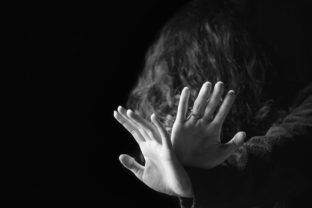 Violence against women. Black and white portrait of scared and desperate woman, focus on the hands in protective gesture