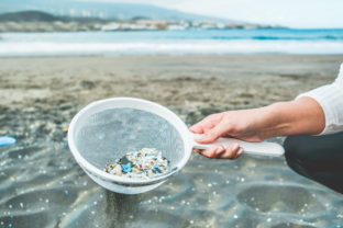 Young woman cleaning microplastics from sand on the beach - Environmental problem, pollution and ecolosystem warning concept - Focus on hand