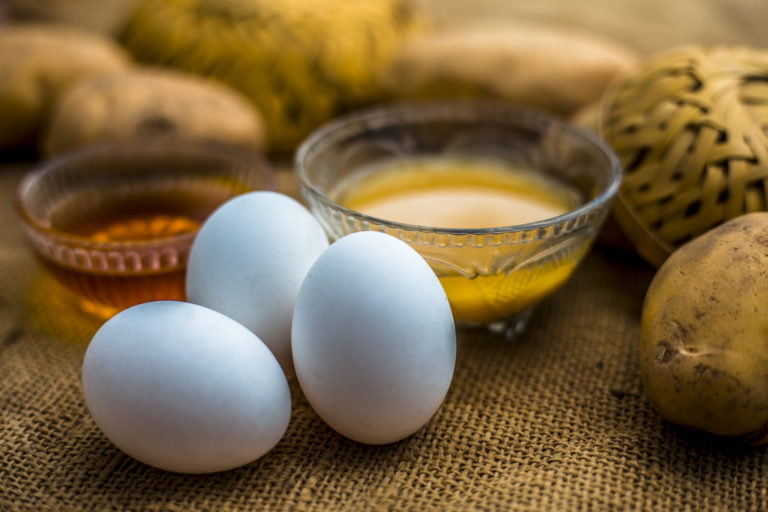 Potato juice plus honey plus egg yolk face mask for dry and damaged hair on the wooden surface along with raw potato, egg and honey present on the surface.