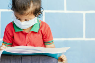 Covid 19 or Coronavirus and Air pollution pm2.5 concept - Little girl wearing medical mask and busy in writing at school - showing Wuhan covid 19 or sars cov 19 outbreak or epidemic of virus.