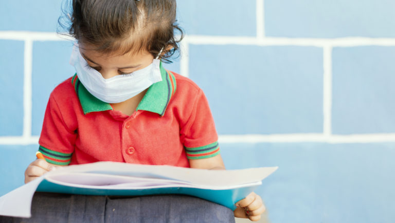 Covid 19 or Coronavirus and Air pollution pm2.5 concept - Little girl wearing medical mask and busy in writing at school - showing Wuhan covid 19 or sars cov 19 outbreak or epidemic of virus.