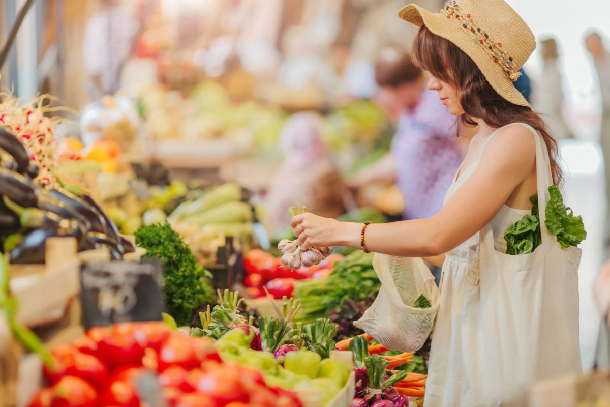 Woman is chooses fruits and vegetables at food market. Reusable eco bag for shopping. Zero waste concept.