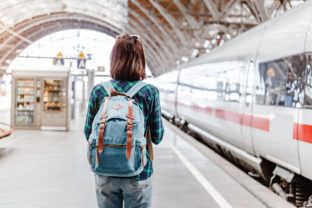 A young tourist girl with backpack waits for train on railway station