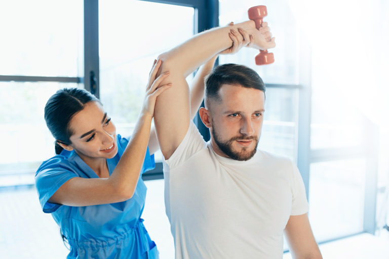Man lift a dumbbell, he doing treatment exercise with his physiotherapist. Physio treatment at rehab center