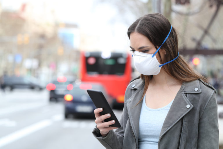 Woman with mask using phone with city traffic background