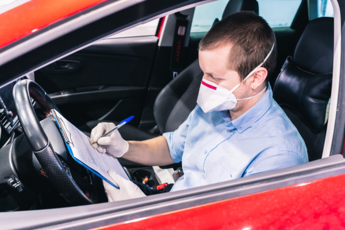 A technician doing a security inspection inside a vehicle protected with a mask and gloves to prevent the spread of virus