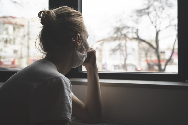 Woman with protection medical face mask by the window