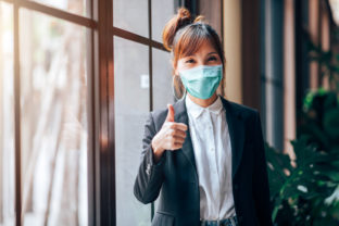Asian Business Woman Standing and Showing Thumbs up in Working Office. She Wearing Virus Protective Mask in Prevention for Coronavirus or Covid 19 Outbreak Situation - Healthcare and Business Concept