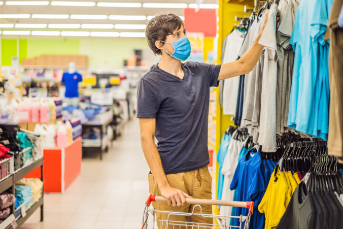 Man in a clothing store in a medical mask because of a coronovirus. Quarantine is over, now you can go to the clothing store