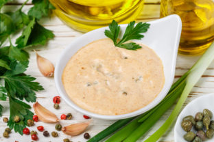 Homemade traditional French remoulade sauce in a White bowl with ingredients capers, parsley, green onion, mustard, fragrant vinegar, olive oil, garlic on a light wooden table. dip. Selective focus