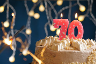 Birthday cake with 70 number pink candles and burning sparkler on blue backgraund. Close up