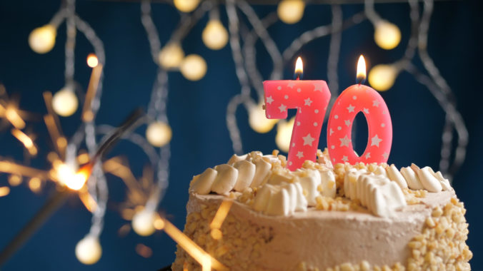 Birthday cake with 70 number pink candles and burning sparkler on blue backgraund. Close up