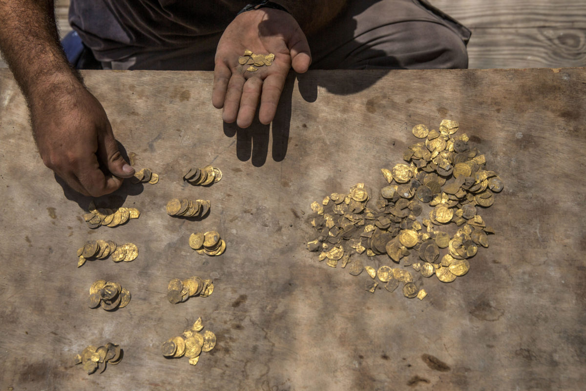 Israeli archaeologist Shahar Krispin counts gold coins buried in a pottery vessel that was discovered at an archeological site in central Israel, Tuesday, Aug 18, 2020. Israeli archaeologists have announced the discovery of a trove of early Islamic gold coins during recent salvage excavations near the central city of Yavn Tel Aviv. The collection of 425 complete gold coins, most dating to the Abbasid period around 1,100 years ago, is a "extremely rare" find. (AP Photo/Sipa Press, Heidi Levine, Pool)
