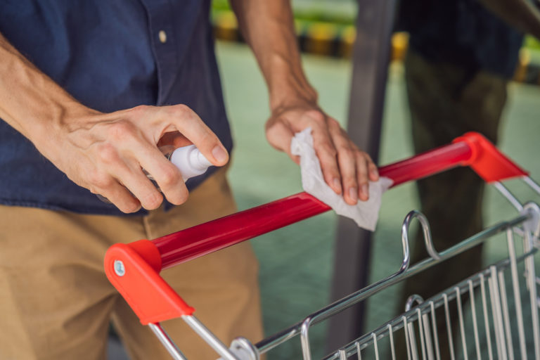 Man hand disinfecting shopping cart with alcohol spray for corona virus or Covid 19 protection