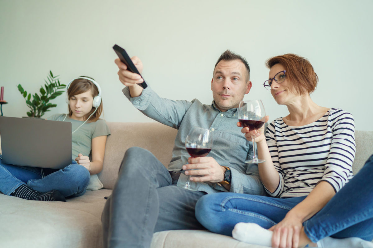 Sad little child listening to music alone while addicted parents drinking alcohol at home. Family Alcoholism problem concept