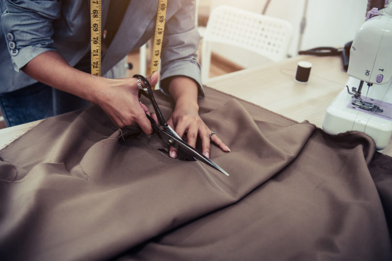 Dressmaker cutting dress fabric on sketch line with sewing machine. Fashion designer tailor or sewer in workshop studio designing new collection clothes. Business owner shop and entrepreneur concept
