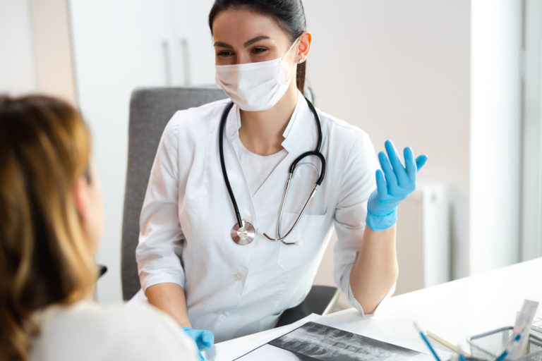 Serious pediatrician in medical mask discussing x ray of spine with mother