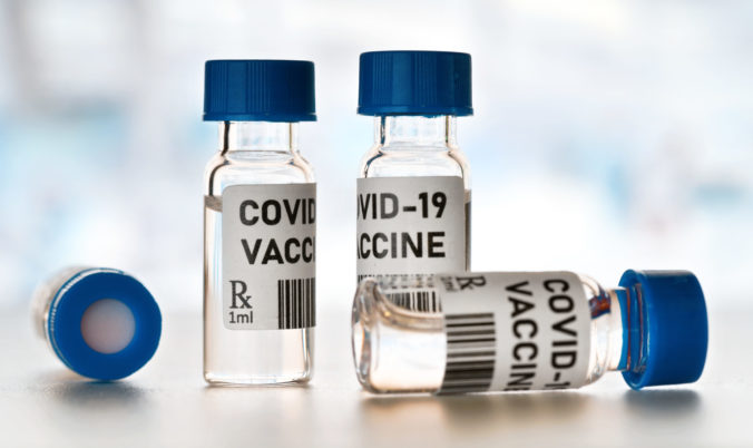 Coronavirus Covid 19 vaccine concept - small glass vials with blue caps on white table, closeup detail (own design - dummy bar code)