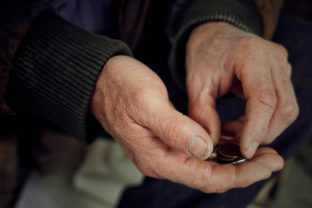 Old hands close up consider coins. Concept of poverty.