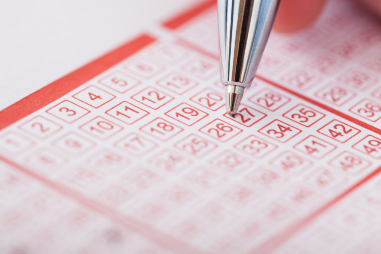 Person Holding Pen Over Lottery Ticket