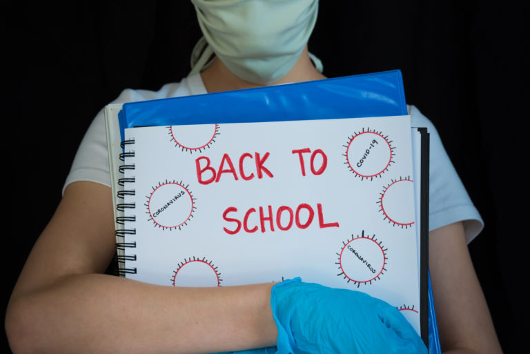 Close up of student wearing face mask and surgical gloves, holding school books with Back to School written on cover