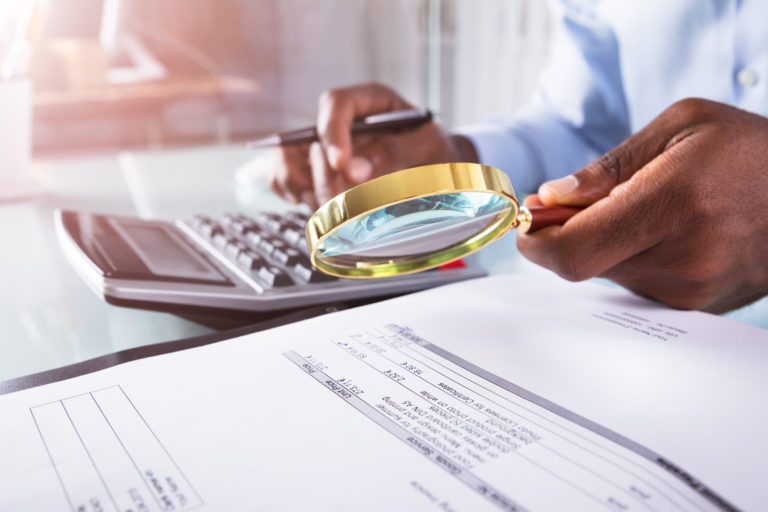 Businessman Holding Magnifying Glass Over Invoice