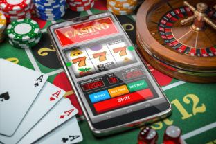 Casino online. Smartphone or mobile phone, slot machine, dice, cards and roulette on a green table in casino.
